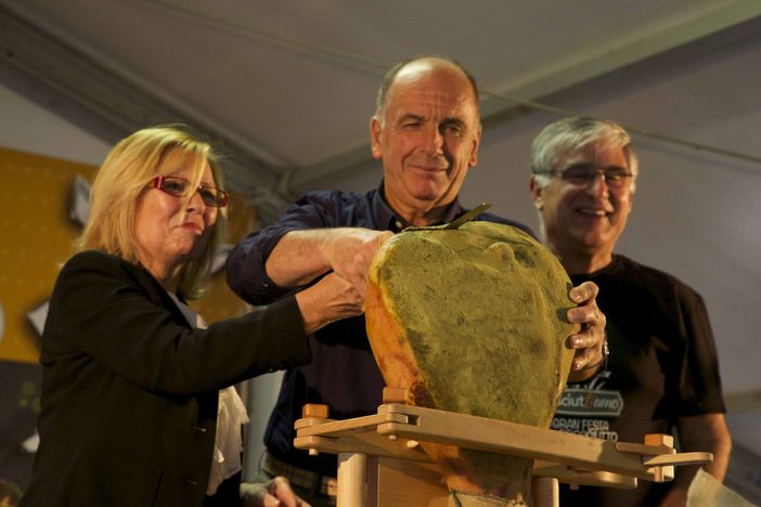 La signora Maria Maione, Augusto Rollandin (al centro) e ùd il signor Paolo Covi inaugurano la prima edizione di Prosciuttiamo. Il tradizionale taglio del nastro è sistituito dal taglio del 'violino'