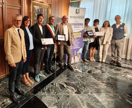 l’Assessore regionale ai Trasporti Luigi Bertschy, l’Assessora al Turismo di Doues Corinne Cuaz, il Vice Sindaco di Doues Daniel Diemoz, il Sindaco di Doues Giorgio Abram, il Presidente della Regione Renzo Testolin, i genitori della minore di Doues, la Coordinatrice l’istituzione scolastica Grand Combin Simona d’Agostino, il Presidente di AICE Valle d’Aosta ODV Manuele Amateis
